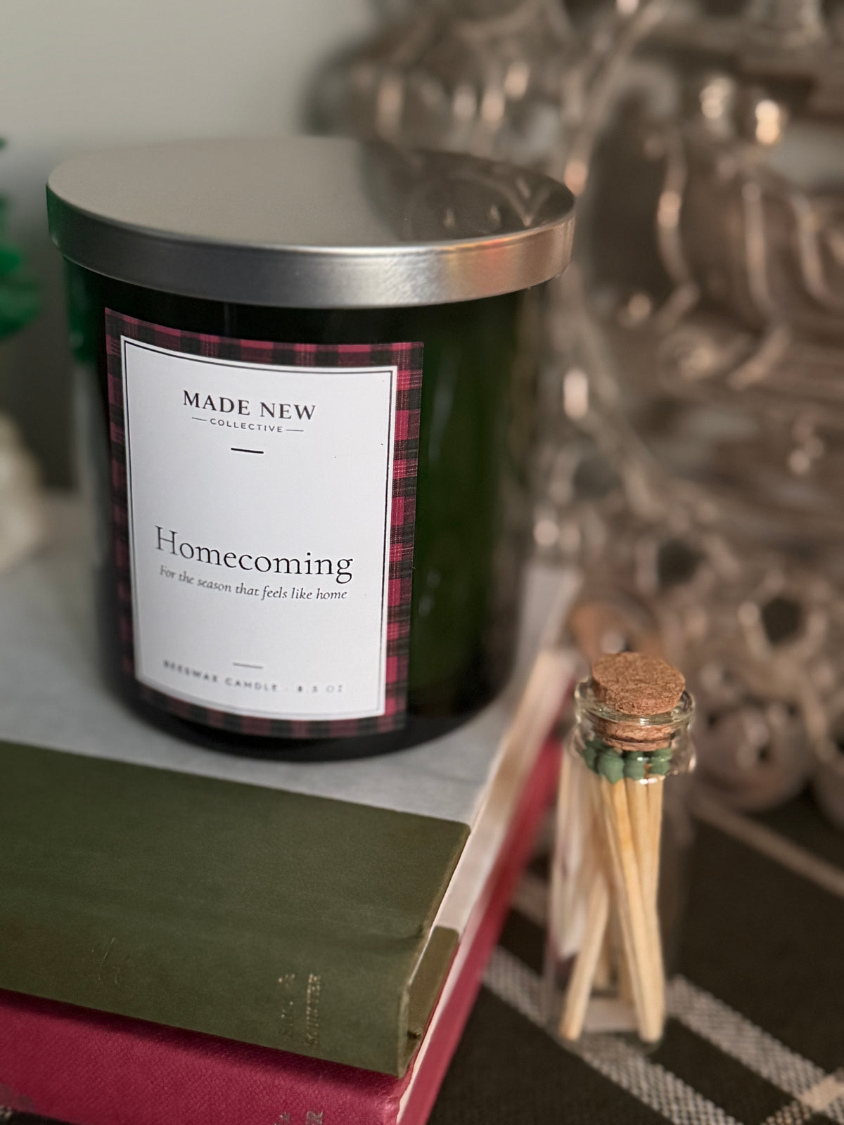Homecoming beeswax candle with silver lid on, sitting on a stack of vintage books next to a Made New Collective glass match jar