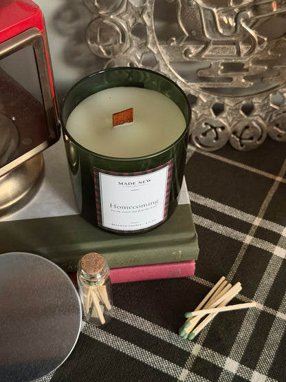Homecoming candle seen from above with the silver lid set aside, resting on a vintage book on a green plaid cloth with loose matches and a Made New Collective match jar